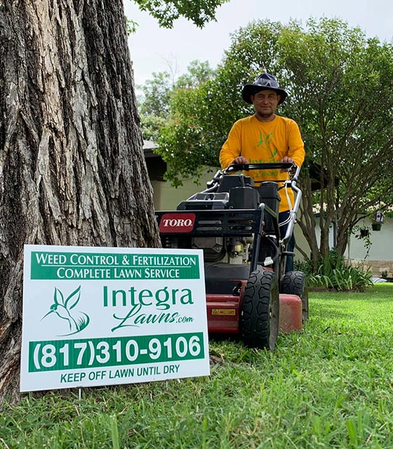 Integra Pest & Lawn professional with mower and signage in a lawn near Fort Worth, TX.